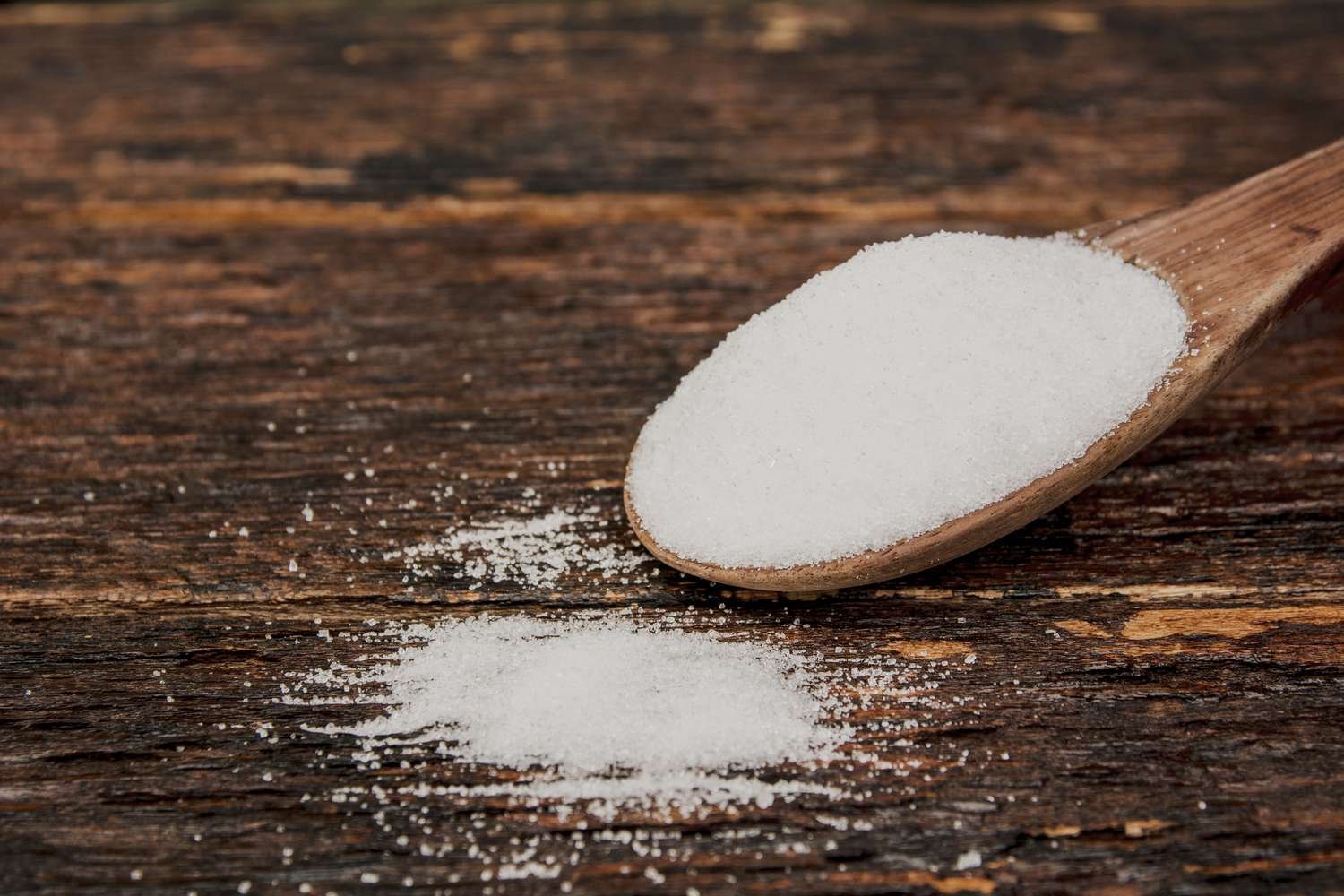 A wooden spoon filled with salt against a wooden table.